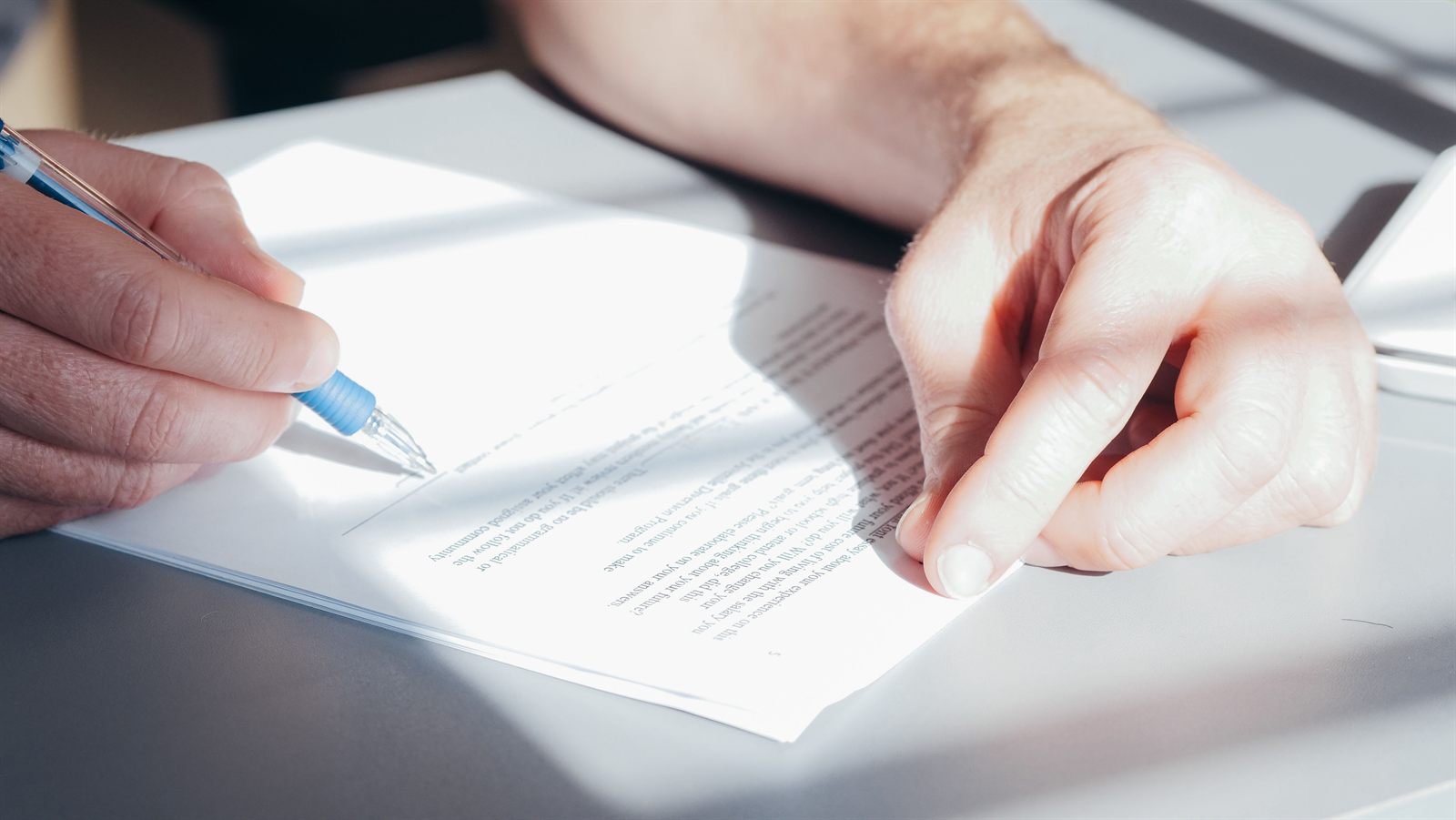 Manos firmando un documento con un bolígrafo azul