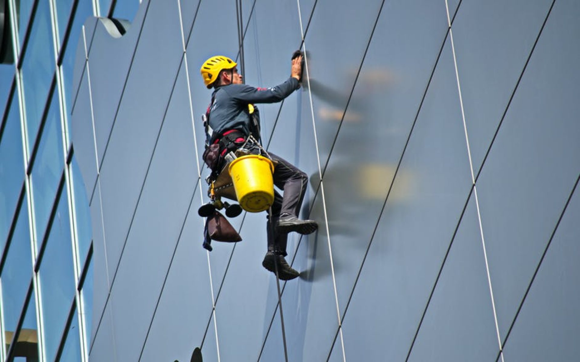 Trabajador con casco amarillo suspendido con cuerdas en la fachada de vidrio de un edificio