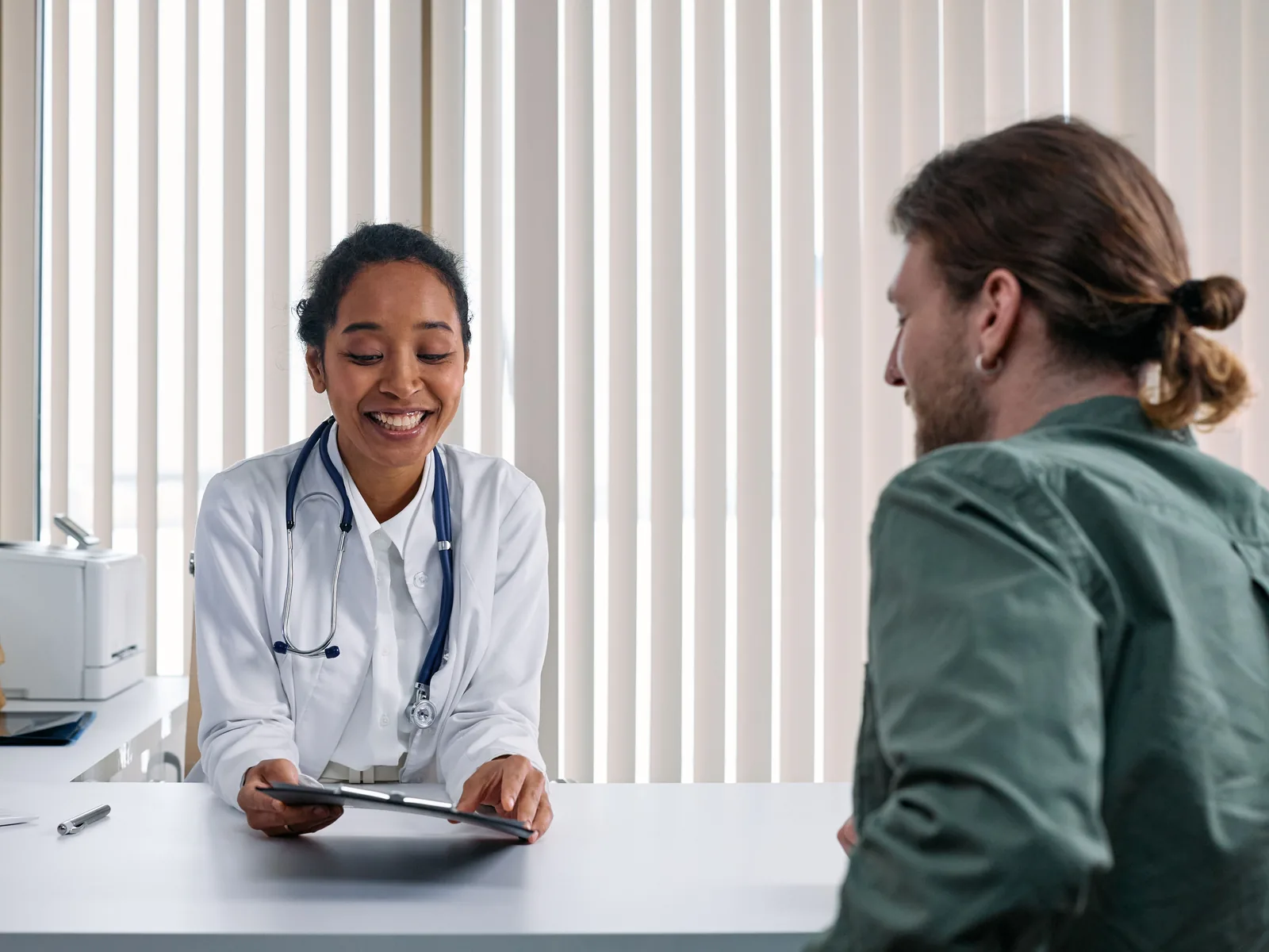 Médica sonriendo mientras atiende a un paciente en un consultorio