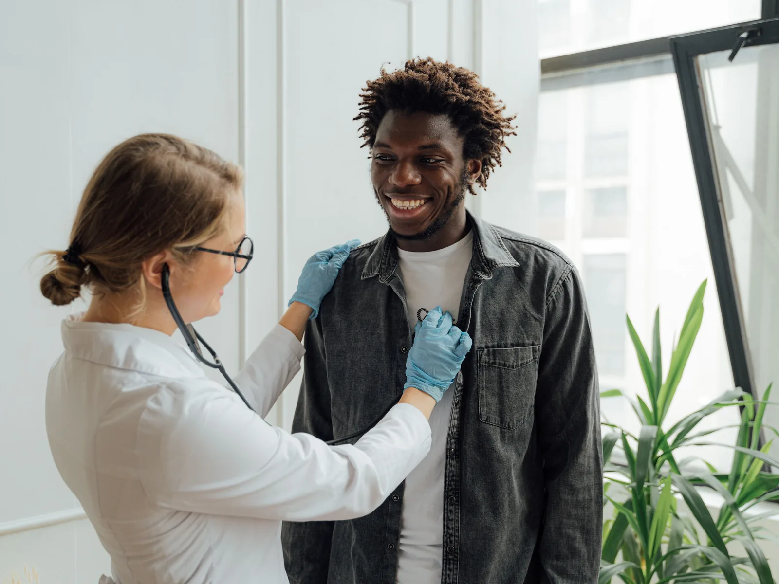 Médica auscultando con un estetoscopio a un joven que sonríe durante una consulta