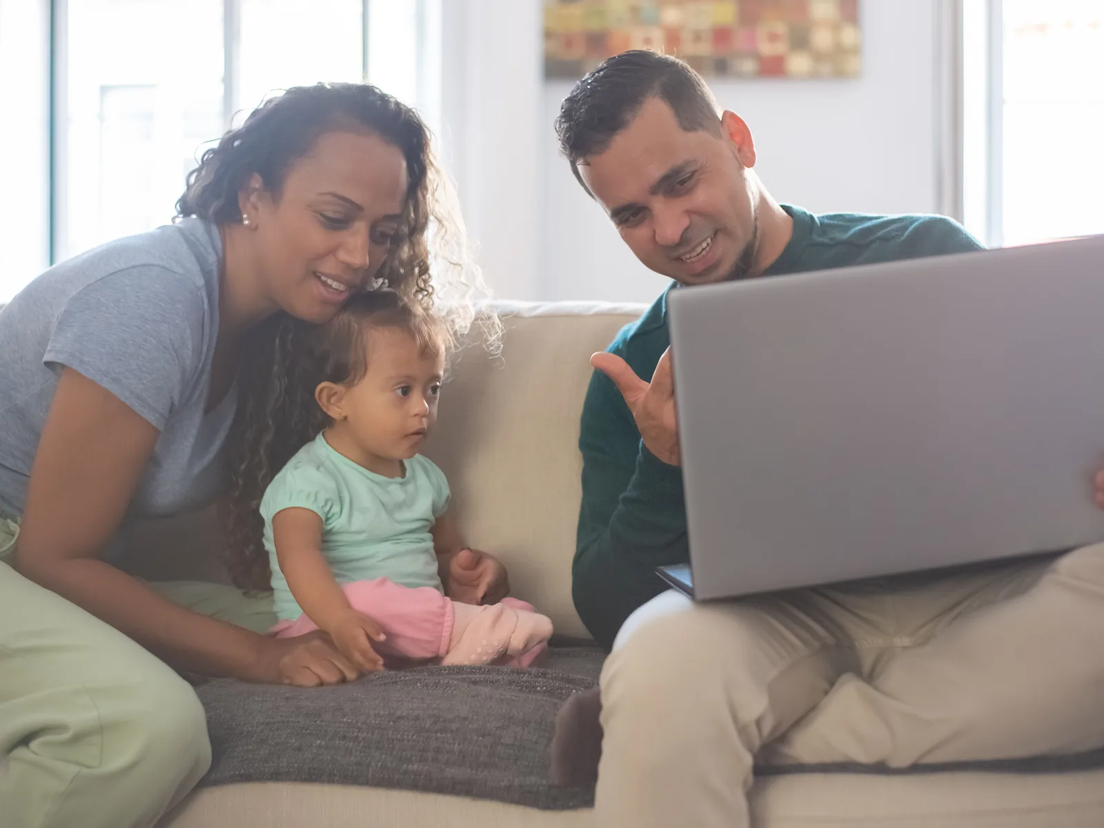 Madre, padre y bebé sonriendo en el sofá de su casa frente a un computador portátil